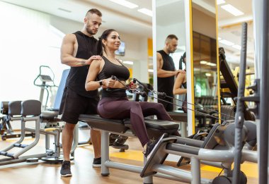Young fit woman training muscles with personal trainer man in the gym