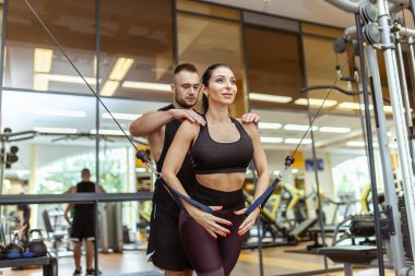 Young fit woman training muscles with personal trainer man in the gym