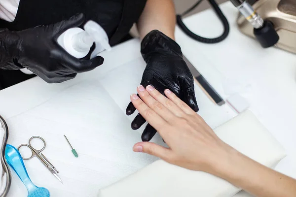 Manicurist workflow with model hands. Hands in black gloves sprays client\'s hands with liquid for manicure