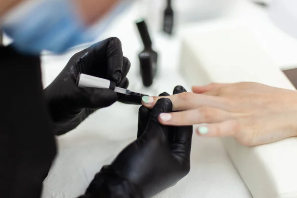 Manicurist paints with nail polish the nails of a woman\'s clint in nail salon. The working process