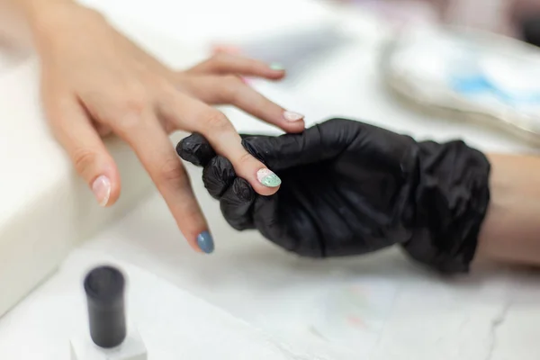 Manicurist paints with nail polish the nails of a woman\'s clint in nail salon. The working process