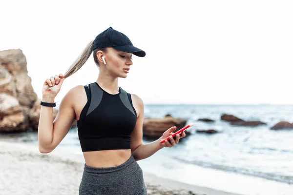 Fit Woman Sportswear Cap Uses Smartphone Wild Beach — Stockfoto