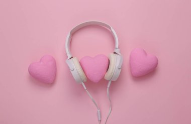 Pembe arka planda kalpleri olan kulaklıklar. Romantik melodi. Üst görünüm