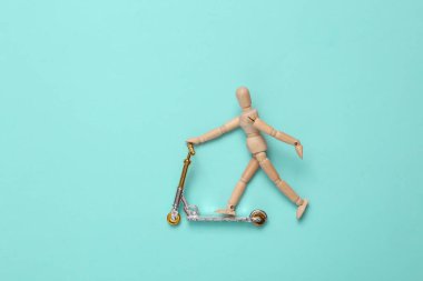 Wooden puppet on a scooter, blue background. Top view