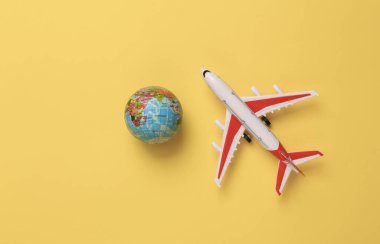 Model airplane with globe on yellow background. Travel concept. Flat lay, top view