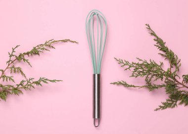 Whisk on a pink background with sprig of fir. Top view, Flat lay