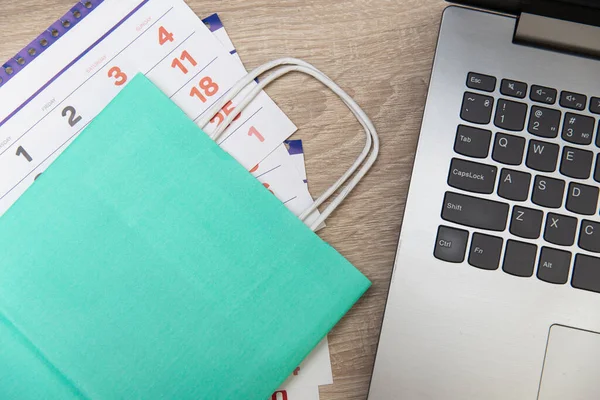 Paper calendar and shopping bag with laptop on wooden table