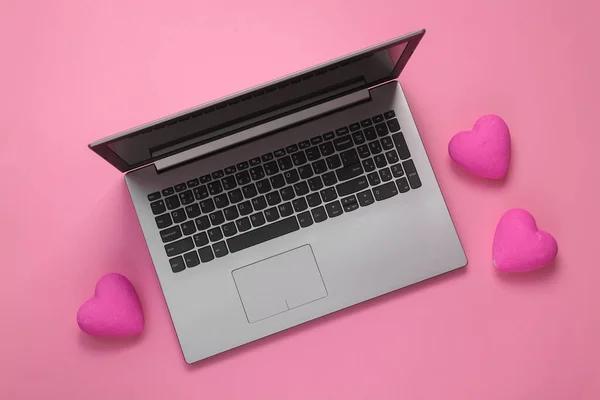 Laptop with pink hearts on a pink background. Flat lay