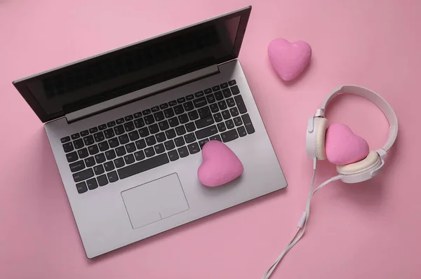 Laptop, headphones with hearts on a pink background. Romantic melody. Top view