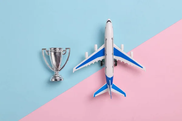 Passenger plane with winner's cup on blue-pink background. Top view