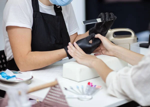 Manicurist files with nail file the nails of hands of woman client in nail salon