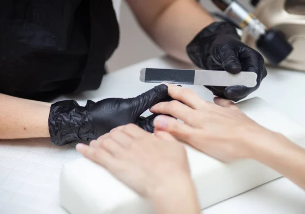 Manicurist files with nail file the nails of hands of woman client in nail salon