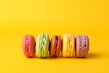Set of colored macaroons isolated on yellow background. French sweet delicacy.