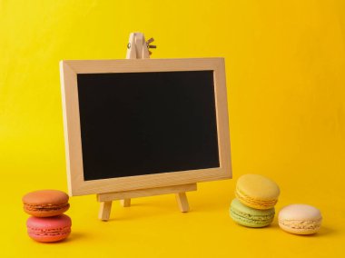 Empty chalk board and french macaroons on yellow background