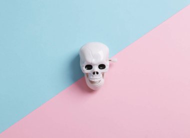 Minimal halloween still life. Clockwork skeleton skull on blue pink background. top view