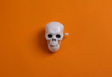 Minimal halloween still life. Clockwork skeleton skull on orange background. Top view