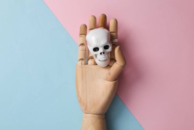 Wooden hand with a skeleton head on a blue pink background. Minimal halloween layout. Top view. flat lay