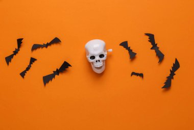 Halloween background with skeleton skull and bats on orange background. Top view. Flat lay