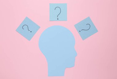 Paper cut head and memo papers with question marks on pink background. Flat lay