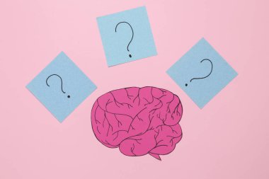 Paper cut brain and memo papers with question marks on pink background. Flat lay