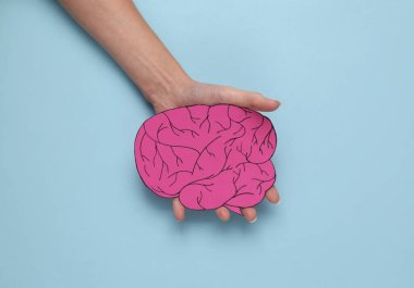Female hand holding a paper-cut brain on a blue background