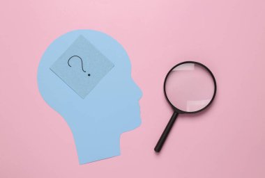 Paper cut Human head with question mark and magnifying glass on pink background. Finding answers to questions