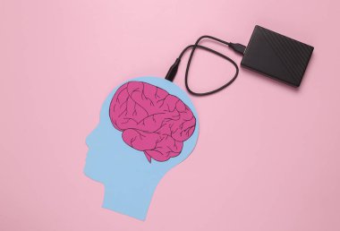 Paper-cut head with brain and external hard drive connected on pink background. Futuristic technologies of digitalization of consciousness. Memory storage