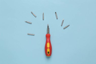 Screwdriver with set of bits on blue pastel background