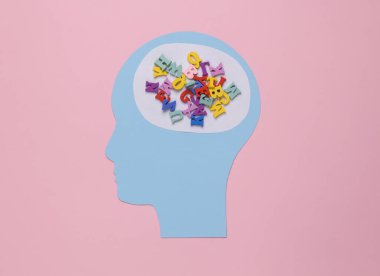 Paper cut head with many letters in place of the brain on a pink background.