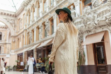 Young fashion woman in a hat walks looking at the architecture of the city