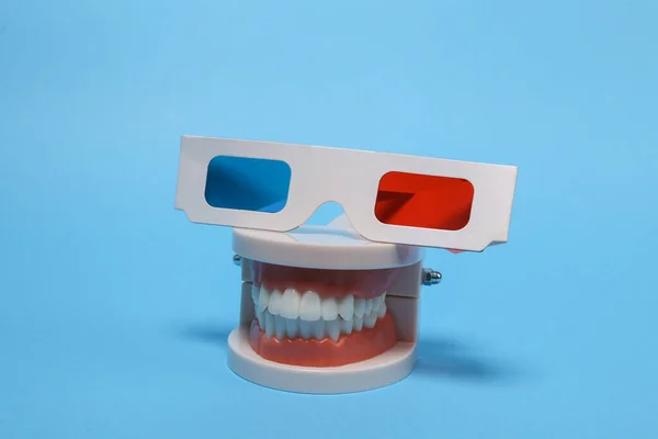 Entertainment concept. Human jaw model with 3d glasses on a blue background