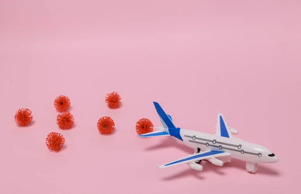 The concept of travel during a pandemic. Airplane model with virus strain molecules on pink background