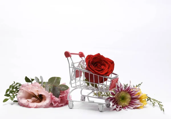 Shopping cart with red rose bud and many different flowers isolated on white background