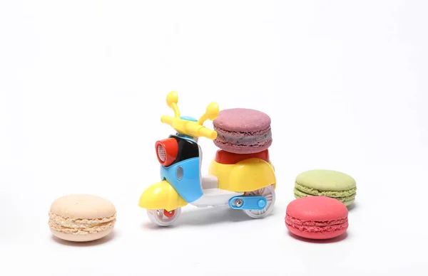 Food delivery concept. Toy moped scooter with french macaroons isolated on white background
