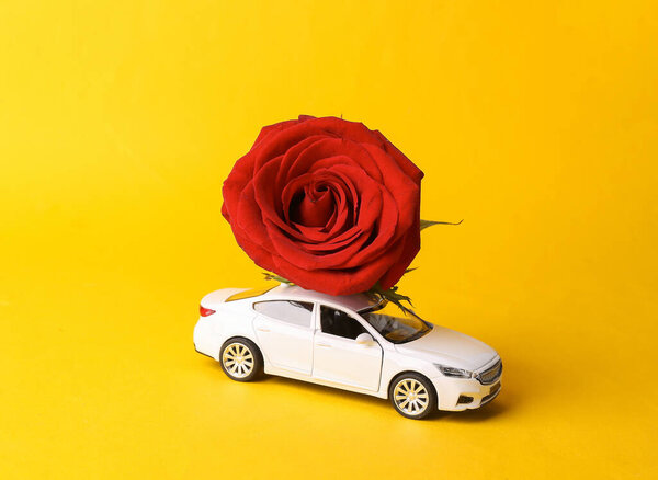 Flower delivery, romantic concept. Valentine's Day. Model car with red rose on yellow background