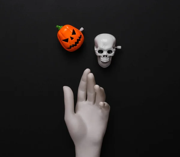 White hand with skeleton head and jack pumpkin on black background. Minimal halloween layout. Top view. flat lay