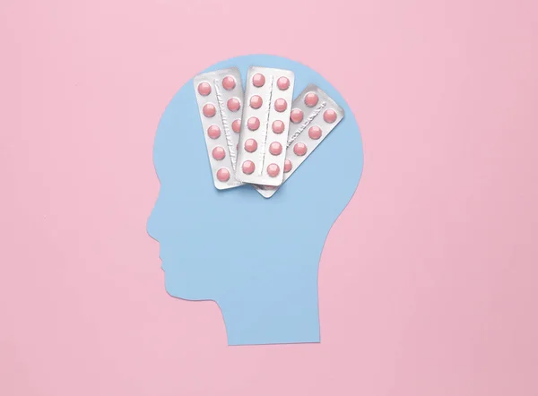 Paper-cut head of a man with pills on a pink background. Headache treatment