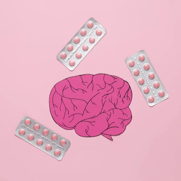 Paper-cut brain with pills on a pink background. Headache treatment