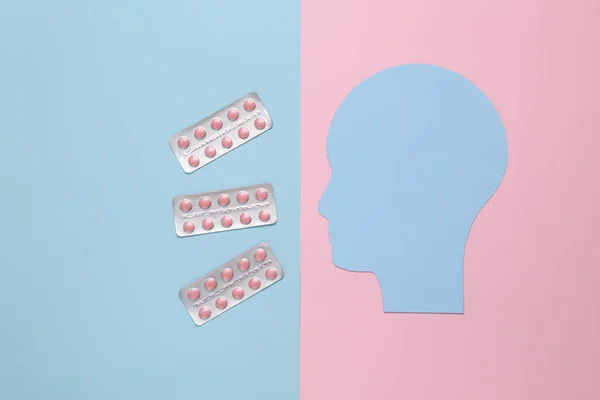 Paper-cut human head with pills on pink blue background. Headache treatment