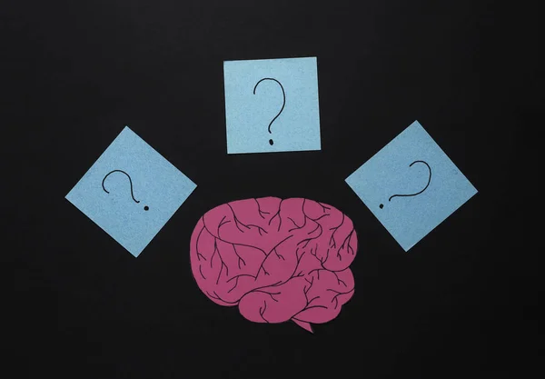 Paper cut brain and memo papers with question marks on black background. Flat lay