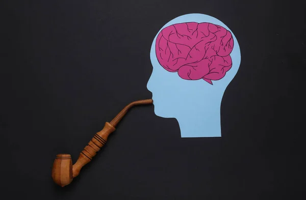 Effect of nicotine on the brain. Cutted head with a brain with a smoking pipe on black background