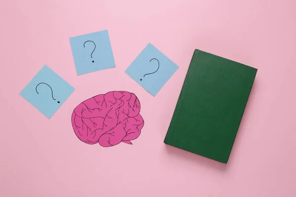 Getting answers to questions. Paper cut brain with question marks and a book on a pink background. New knowledge, learning concept. Creative layout