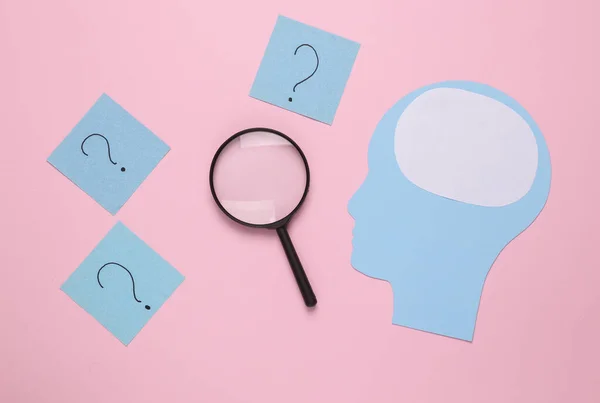 Paper cut Human head, question marks and magnifying glass on pink background. Finding answers to questions