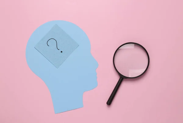 Paper cut Human head with question mark and magnifying glass on pink background. Finding answers to questions