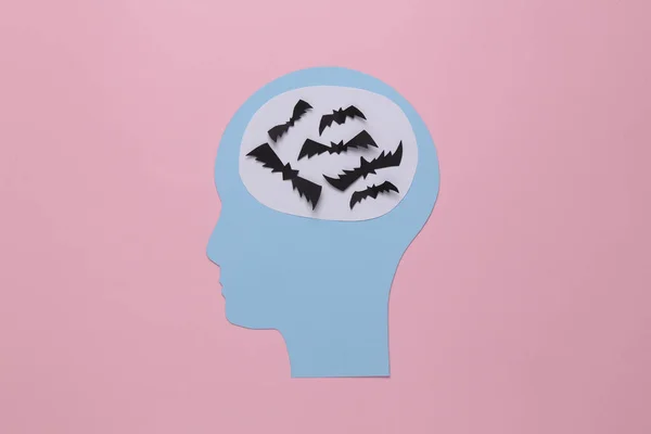 Paper cut head with bats instead of a brain on a pink background. Scarcity of ideas concept