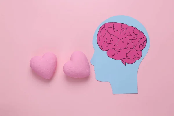 Paper-cut head with brain and hearts on pink background. Falling in love concept