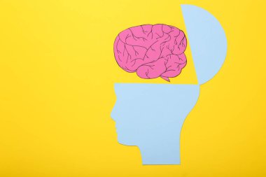 Zihnini aç, zihinsel sağlık kavramı, yaratıcı düşünce. Sarı arka planda insan kafası ve beyninin kağıt silueti.