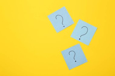 Sarı arka planda soru işaretleri olan not kağıtları. İş, psikoloji, soru kavramına yanıtlar