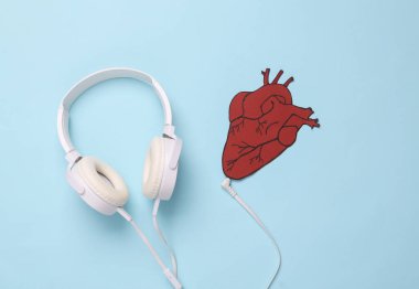 Kalbinin sesini dinle. Kulaklıklar mavi arka plandaki anatomik kalbe bağlı. Üst Manzara. Düz yatıyordu