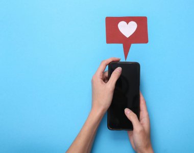 Eller, mavi arka planda bildirim simgesi olan akıllı telefonu kullanır. Sosyal medya. Beğeni, takipçiler geri bildirim